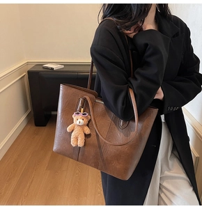 Detail of vintage brown tote bag with bear charm and sleek leather texture for women