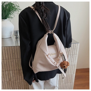 Détail du sac à dos crème au design géométrique, logo doré et pendentif en peluche