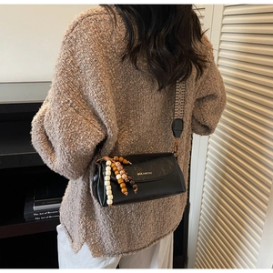 Detail of black leather crossbody bag featuring wide jacquard strap and beaded charm