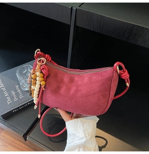 Detail of burgundy suede dumpling bag with elegant beaded tassel and zipper hardware