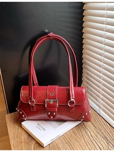 Vintage dark red leather underarm bag with silver buckles and studs on wooden table