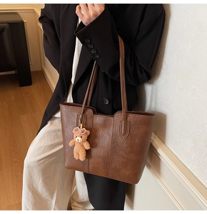 Detail shot of vintage brown leather tote bag with a cute plush bear charm on shoulder