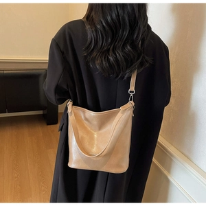 Détail du sac à bandoulière en cuir beige souple au grain fin porté sur un manteau noir