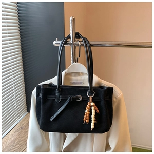 Detail of black suede tote bag featuring decorative metallic eyelets and wooden bead tassel