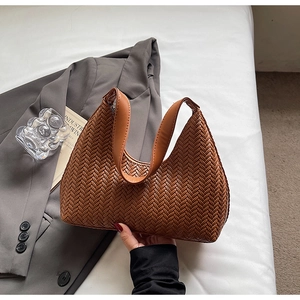 Dettaglio della trama in pelle intrecciata di una borsa hobo marrone tenuta da modella