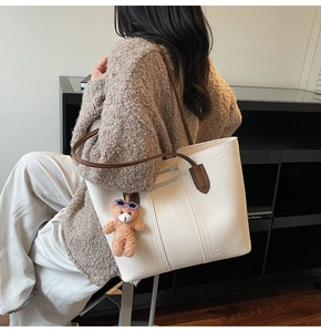 Detail of white leather tote bag featuring a cute teddy bear charm and brown handles