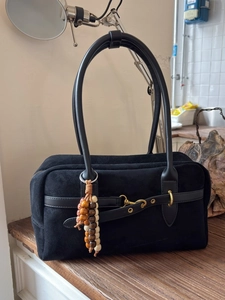 Elegant black suede Boston handbag with premium leather handles and beaded charm on wood