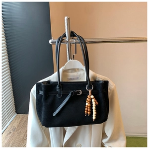 Detail of black suede tote bag with decorative buckle and wooden bead pendant accessory