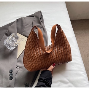 Dettaglio macro della trama intrecciata marrone e del manico in pelle di una borsa hobo