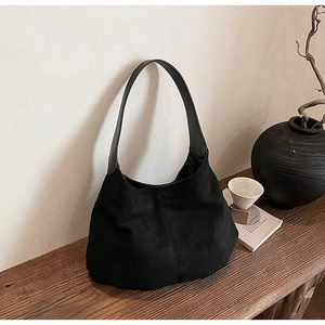 Close-up of black matte suede tote bag on a rustic wood surface with home decor props