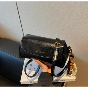 Close-up of black retro leather shoulder bag featuring beaded tassel and golden hardware