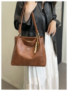 Detail of a brown leather shoulder bag featuring beaded tassel and vintage texture