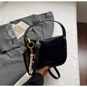 Détail du sac à main en cuir mat noir et suède avec breloque en perles de bois colorées