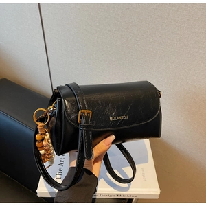 Detail of black glossy leather bag with gold buckle and beaded charm accessory
