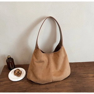 Detail shot of a caramel suede hobo bag placed on a rustic wooden desk with warm lighting