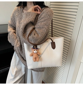 Cream leather tote bag with brown straps and cute teddy bear charm on model shoulder