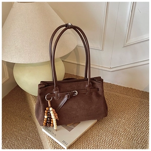 Detail of dark brown matte tote bag with decorative bead charm on a magazine