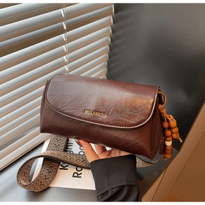 Detail of dark brown faux leather crossbody bag with wide strap and beaded charm