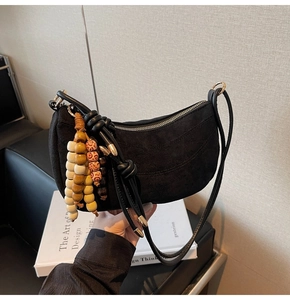 Detail of black faux suede crescent bag featuring vintage wooden bead tassel and leather strap