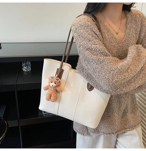 Detail of off-white faux leather tote bag with brown straps and cute bear charm