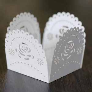 Detailed laser-cut white rose pattern paper cake wrapper on dark wood background