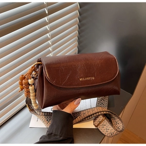Detail of vintage brown shoulder bag with rainbow woven strap and wooden bead charm