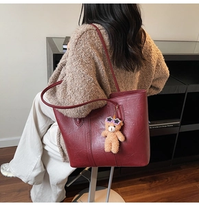 Detailed view of dark red leather tote bag with a cute plush bear charm on a shoulder strap