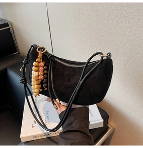 Detail of black suede crescent bag with vintage beaded charm and knotted strap accent