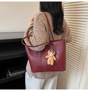 Detail of deep red glossy tote bag with a cute bear charm and precise stitching