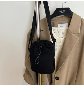 Detail of black mini crossbody bag with drawstring closure and adjustable strap