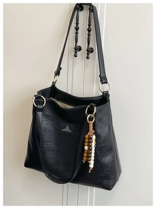 Close-up of black lychee texture leather tote with decorative wood bead tassel detail