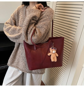 Detail of burgundy leather tote bag featuring a brown teddy bear charm on shoulder strap