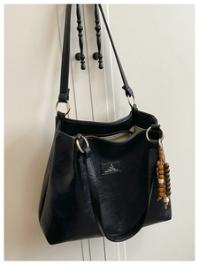 Detail of black faux leather tote with wooden bead charm and brand patch on white door