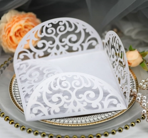 Close-up of laser-cut white wedding invitation with elegant floral scroll patterns