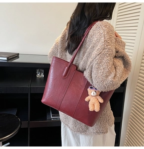 Detailed view of wine red vintage tote bag with plush bear charm on model shoulder