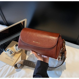 Detail of vintage brown leather pillow bag with wide patterned strap and beaded charm