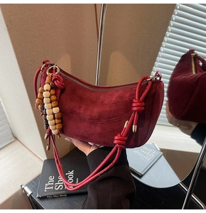 Close-up of dark red suede crescent bag with gold zipper and wooden bead tassel