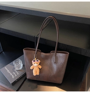 Detail of dark brown vintage tote bag with retro leather texture and plush bear charm