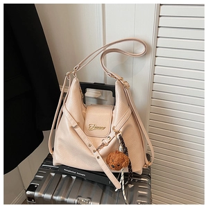 Gros plan d'un sac hobo en similicuir beige avec un charme d'ourson sur une valise argentée