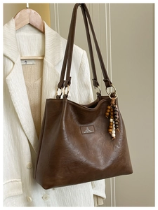 Detail of vintage brown leather tote bag featuring a brand patch and beaded pendant