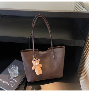 Detailed view of a dark brown faux leather tote bag with a cute teddy bear charm