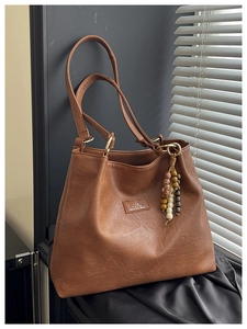 Close-up of vintage brown tote bag with leather logo patch and beaded tassel detail