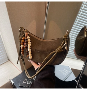Detail of dark olive green suede crescent bag with wooden bead tassel and mirror reflection