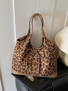 Large leopard print tote bag with brown handles and bow detail on a leather seat