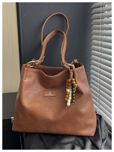 Close-up of brown textured leather tote with wooden bead tassel and metallic zipper