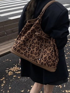 Large leopard print tote bag with leather straps worn by model on an autumn city street