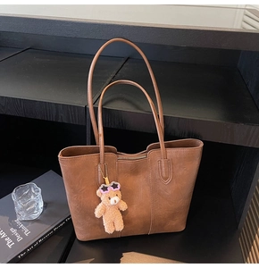 Detail of a brown leather tote bag with a cute plush bear pendant and zipper closure