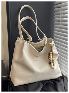 Detail of minimalist cream tote bag showing grainy faux leather texture and golden rings