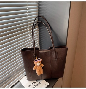 Detail of dark brown tote bag with pebble texture and cute teddy bear charm