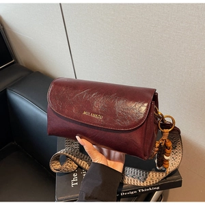 Detail of burgundy retro leather bag with patterned wide strap and beaded charm